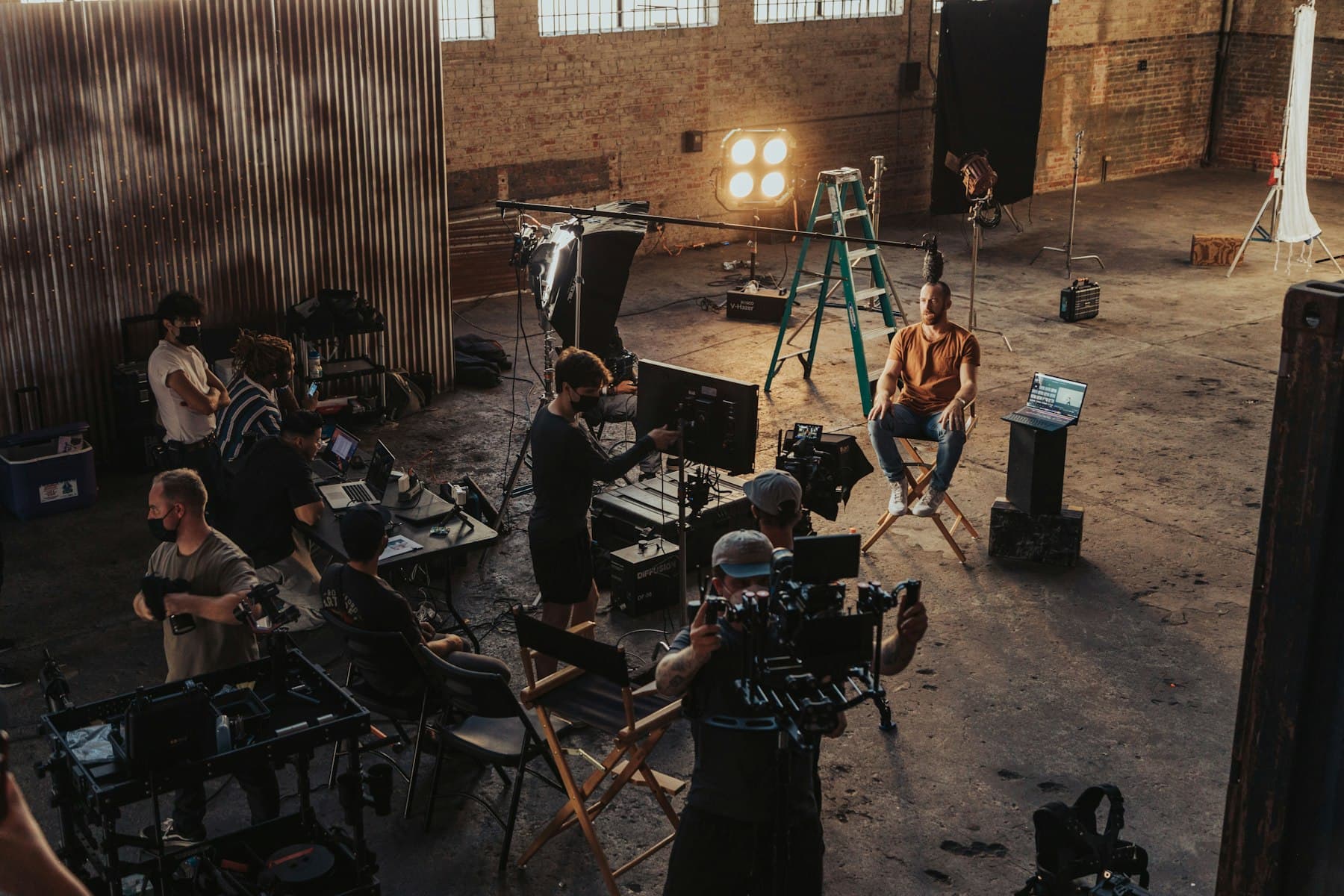 Film crew directing talent seated in a director's chair on a commercial set with cinema cameras, boom and lighting